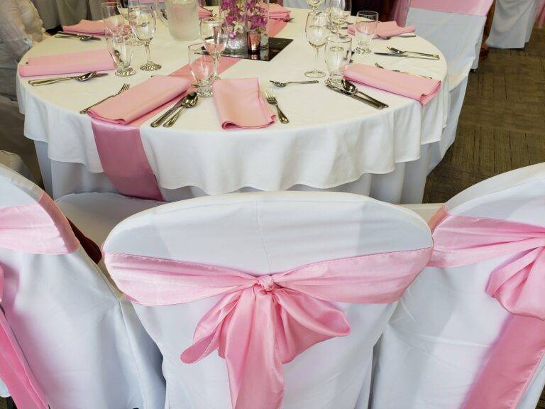 Party tables decorated in crisp white linens and pink silk ribbons ready for celebration