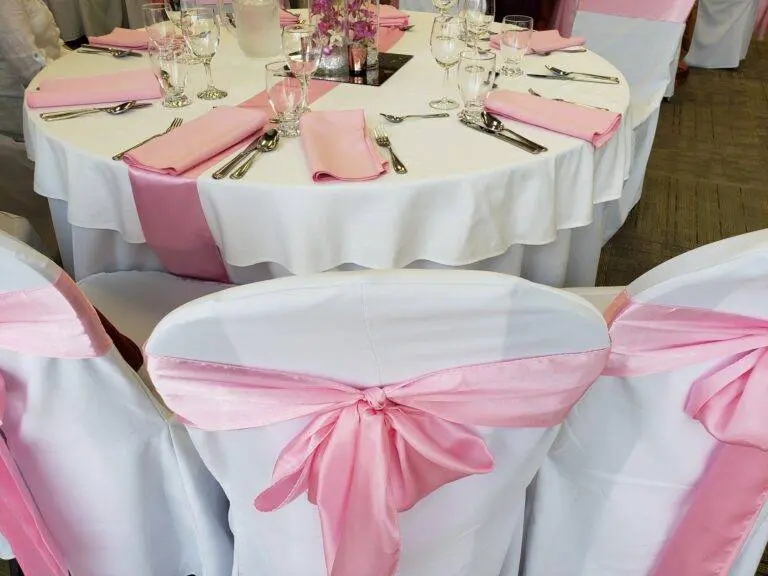 Party tables decorated in crisp white linens and pink silk ribbons ready for celebration